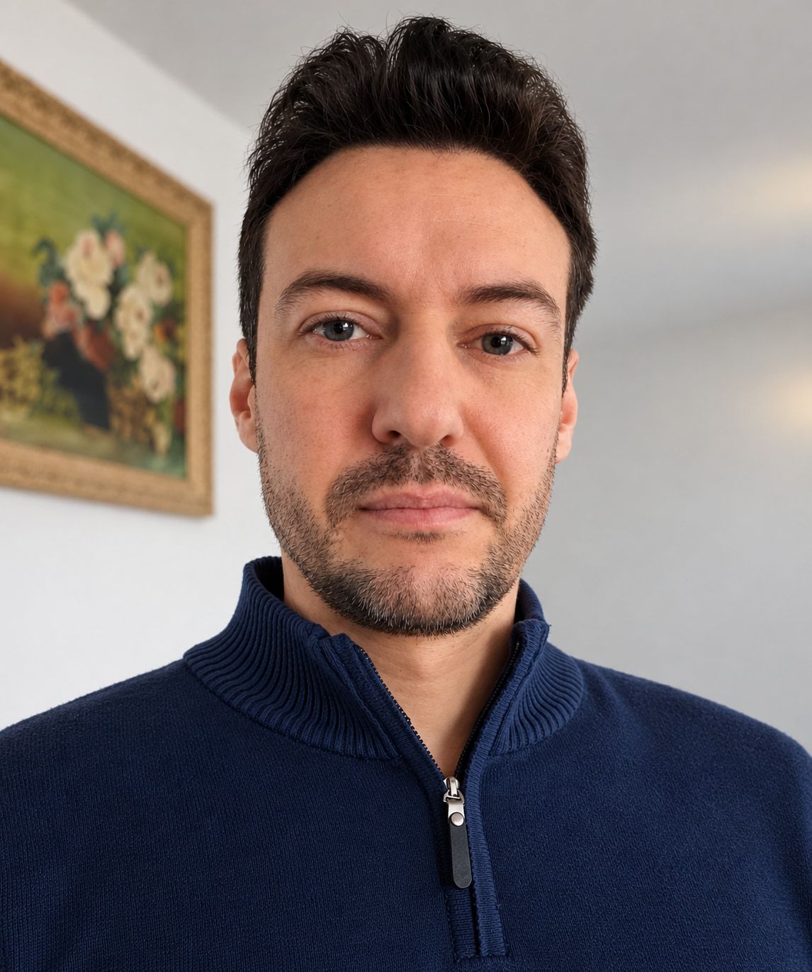 Portrait of Raphael Bohrer in a navy sweater in front of a flower painting
